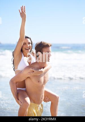 Spaß in der Sonne mit meiner Liebe. Eine Frau und ein Mann am Strand mit dem Mann, der der Frau einen Huckepack gab. Stockfoto
