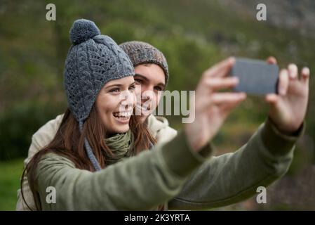 Wir müssen diese Ansicht bekommen. Ein junges Paar, das während einer Wanderung in den Bergen ein Foto gemacht hat. Stockfoto