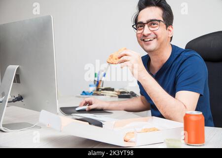 Mann chillen Essen, während er arbeitet und auf seinem Arbeitsplatz im Internet surft. Stockfoto