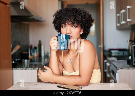Transgender Frau trinkt eine Tasse Kaffee in der Küche zu Hause sitzen. Stockfoto