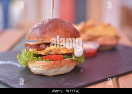 Burger-Menü mit Ei, Huhn, Rindfleisch, Tomaten und Salat auf dem schwarzen Schiefertafel Stockfoto