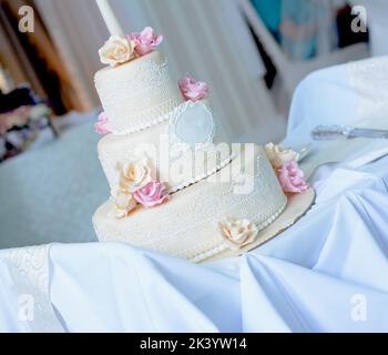 Weiße Hochzeitstorte mit Spitze und rosa und beigen Rosen auf der Oberseite Stockfoto