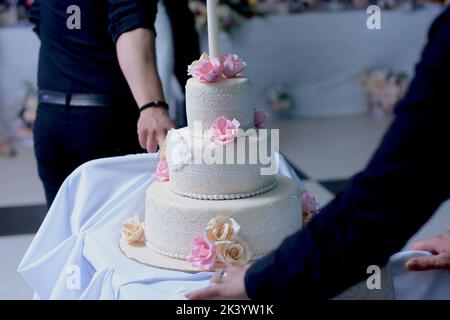 Ein mehrstufiger weißer Hochzeitstorte mit Spitze und rosa und beigen Rosen auf der Oberseite Stockfoto