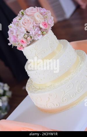 Elfenbeinfarbene Hochzeitstorte mit einem Blumenstrauß darauf Stockfoto