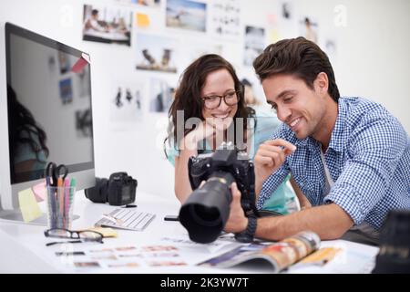 Die Entscheidung für das perfekte Bild...zwei junge Fotografen, die sich Fotos auf einer Digitalkamera in ihrem Studio ansehen. Stockfoto