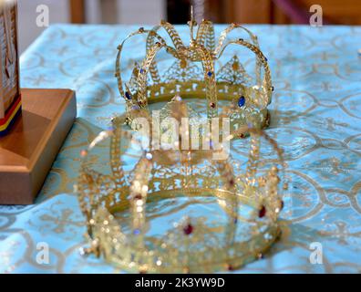 Zwei goldene Krone mit Edelsteinen auf roter Serviette auf Altar in der Kirche. Traditionelle Hochzeitszeremonie. Religion Stockfoto