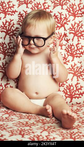 Was für ein neugieriger kleiner Kerl. Ein entzückender kleiner Junge, der in einer Windel sitzt und mit einer Brille spielt.