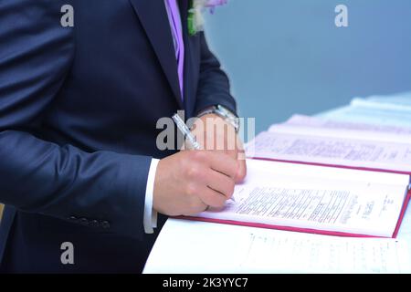 Der Bräutigam unterschreibt die Ehedokumente. Stockfoto