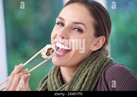 So wirf ich. Eine junge Frau lächelt, während sie ein Stück Sushi in der Hand hält. Stockfoto