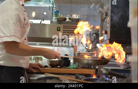 Meeresfrüchte mit Flamme in einer professionellen Küche gekocht. Der Koch wird von einer Seite fotografiert. Stockfoto