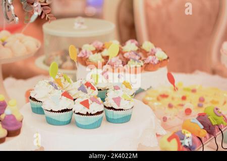 Weiße cremefarbene Muffins, verziert mit buntem dreieckigem Marzipan. Süßigkeitenbar Stockfoto