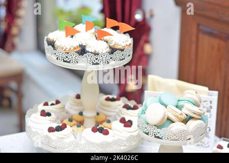 Weiße und blaue Macarons auf Tablett und Cupcakes Hintergrund. Süßigkeitenbar Stockfoto