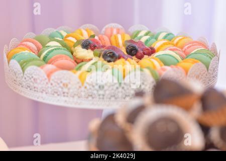 Platte mit bunten Macarons und Minitörtchen mit Frucht- und Vanillecreme in der Mitte Stockfoto