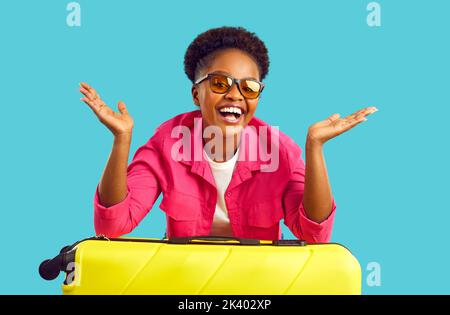 Porträt einer glücklichen, aufgeregten Frau mit Händen auf einem gelben Koffer in rosa Hemd und Brille. Stockfoto