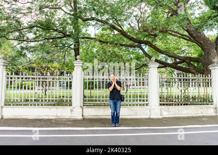 Das Asian Black T-Shirt steht nachmittags vor dem weißen Vintage-Zaun neben der Straße. Stockfoto