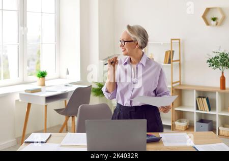Die leitende Geschäftsfrau im Büro nutzt die Spracherkennungsfunktion oder den virtuellen Assistenten auf dem Mobiltelefon. Stockfoto