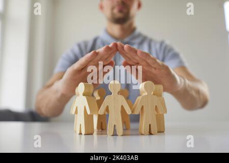 Mann, der seine Hände über menschlichen Holzfiguren hält, als Metapher für Sicherheit und Schutz Stockfoto