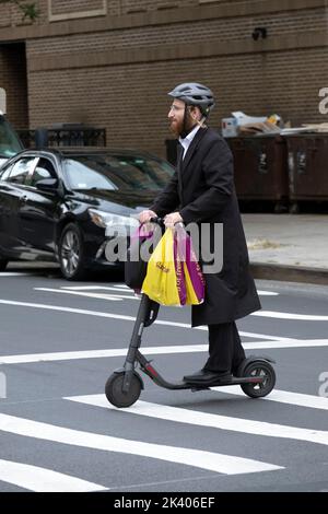 Am Tag vor dem jüdischen Neujahr geht ein orthodoxer Mann mit langem Peyus einkaufen und fährt mit seinem Elektroroller. In Williamsburg, Brooklyn, NYC. Stockfoto