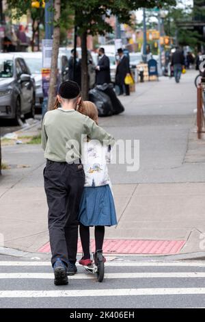 Ein anonymer chassidischer jüdischer Teenager lehrt seine Schwester, wie man einen Roller fährt. Auf der Lee Avenue in Williamsburg, Brooklyn, New York. Stockfoto