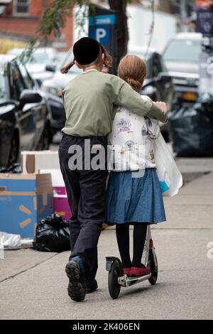 Ein anonymer chassidischer jüdischer Teenager lehrt seine Schwester, wie man einen Roller fährt. Auf der Lee Avenue in Williamsburg, Brooklyn, New York. Stockfoto