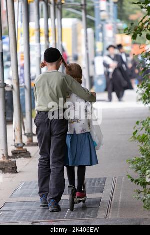 Ein anonymer chassidischer jüdischer Teenager lehrt seine Schwester, wie man einen Roller fährt. Auf der Lee Avenue in Williamsburg, Brooklyn, New York. Stockfoto