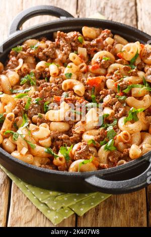 Comfort Food Hackfleisch mit Zwiebeln, Tomatensauce und Makkaroni in der Pfanne auf dem Holztisch gekocht. Vertikal Stockfoto