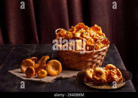 Frische Pfifferlinge, die im Wald, in einem Weidenkorb und auf einem hölzernen Hintergrund gesammelt wurden. Stockfoto