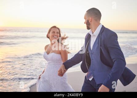Ehepaar, Hochzeit und Strand lächeln bei Sonnenuntergang auf einem romantischen Spaziergang nach der Hochzeit. Glücklich, Frau und Mann in Anzug zu Fuß am Meer, Romantik und Stockfoto
