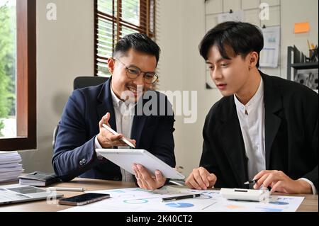 Zwei professionelle und intelligente asiatische Geschäftsleute oder männliche Finanzanalysten diskutieren und arbeiten gemeinsam an ihrem Finanzinvestitionsplan. Stockfoto