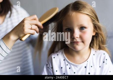 Mutter macht Frisur zu Mädchen Kind auf dem Bett im Schlafzimmer sitzen. Stockfoto