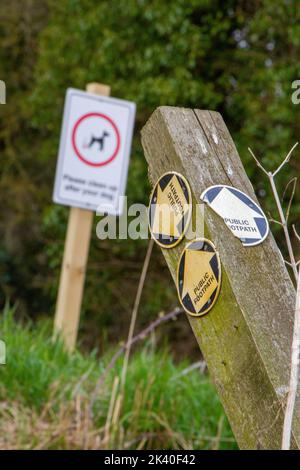 Zwei Schilder, darunter ein einstürzender Posten mit Pfeilen zum öffentlichen Fußweg Stockfoto