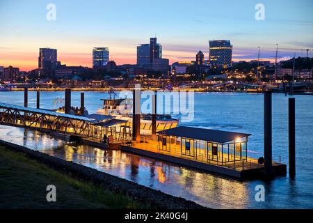 Anlegestelle für die Hafenfähre am Theater im Hamburger Hafen an der Elbe am Abend vor der Skyline der Stadt, Deutschland, Hamburg Stockfoto