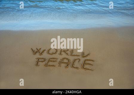 Weltfrieden steht im Sand am Strand, das Meer spült die Küste. Stockfoto