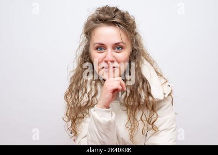 Frau macht eine leisende Geste, indem sie ihren Finger auf ihre Lippen hebt, während sie um Schweigen bittet oder um deine Hilfe bei der Aufbewahrung eines geheimen Stockfotos Stockfoto