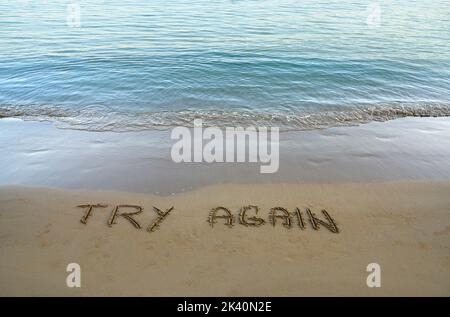 Versuchen Sie es noch einmal in den Sand am Strand geschrieben, mit dem Meer, das die Küste spült Stockfoto