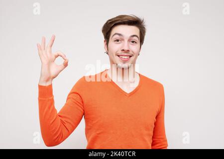 Porträt eines jungen Mannes mit einem OK-Schild mit einem großen Lächeln auf seinem Gesicht, auf weißem Hintergrund Stockfoto Stockfoto