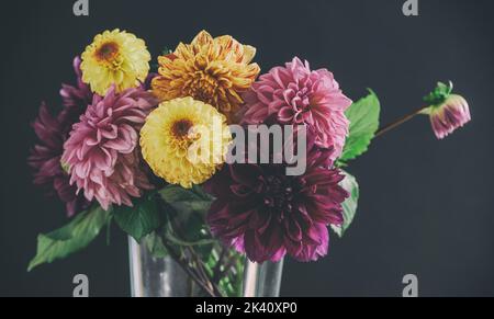 Ein Bukett aus bunten Dahlia-Blumen in einer Glasvase auf schwarzem Hintergrund Stockfoto