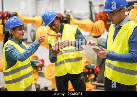 Multirassische Ingenieure, die in der Roboterfabrik arbeiten - Weiche Konzentration auf die rechte Menschenhand Stockfoto