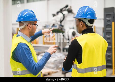 Multiethnische Ingenieure, die in einer Roboterfabrik arbeiten - konzentrieren Sie sich auf den Hardhut des linken Mannes Stockfoto