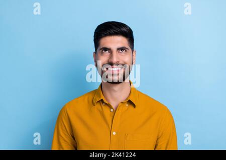 Porträt eines jungen, gut aussehenden, lächelnden Mannes, gekleidet, gelbes Hemd, der auf einen leeren Raum schaut, der auf blauem Hintergrund isoliert ist Stockfoto