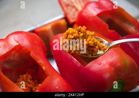Nahaufnahme eines Löffels voller Reis, zubereitet mit Tomaten und Fleisch, das in einem roten Pfeffer gekocht werden soll Stockfoto