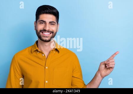 Foto von fröhlich positiv strahlend toothy Mann tragen gelbes Hemd lächelnd zeigt auf leeren Raum isoliert auf blauem Hintergrund Stockfoto