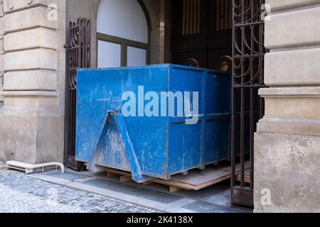 Großer, blauer Müllcontainer aus Metall, der in der Nähe einer Baustelle mit Bauabfällen gefüllt ist. Stockfoto