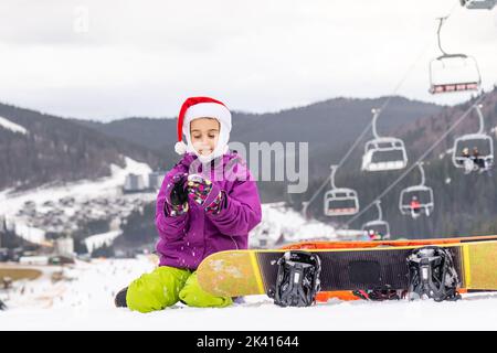 Glückliches Mädchen in santa Hut mit Snowboard Stockfoto