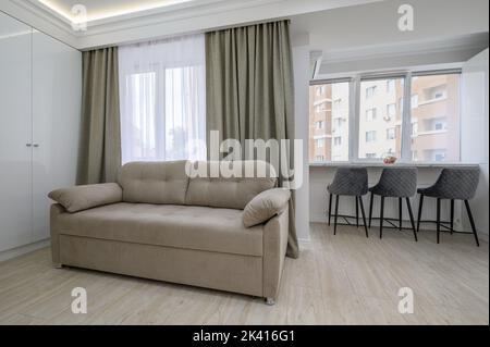 Kleines Studio-Apartment-Wohnzimmer mit einer Couch und einer Essecke am Fensterbrett Stockfoto