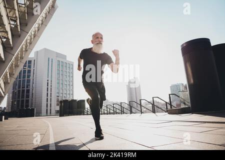 In voller Länge Körpergröße Ansicht von attraktiven leistungsstarken erfolgreich motivierten älteren grauhaarigen Mann läuft auf Gebäude im Freien Stockfoto