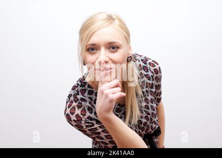 Frau macht eine leisende Geste, indem sie ihren Finger auf ihre Lippen hebt, während sie um Schweigen bittet oder um deine Hilfe bei der Aufbewahrung eines geheimen Stockfotos Stockfoto