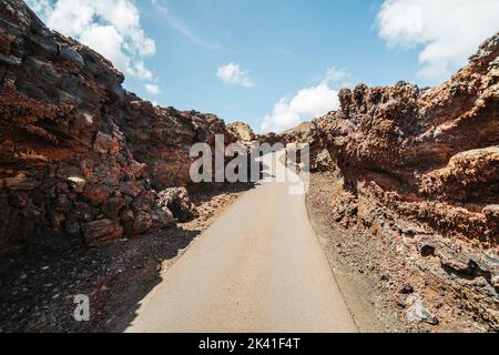 Asphaltstraße in vulkanischer, arider Landschaft des Timanfaya-Nationalparks, Lanzarote, Kanarische Inseln, Spanien Stockfoto