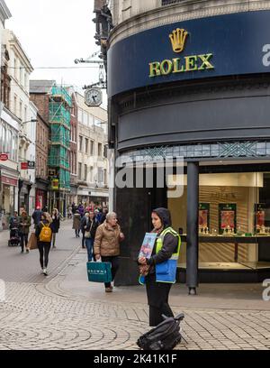 York, North Yorkshire, Großbritannien, September 29 2022. Porträt einer Verkäuferin des Big Issue Magazine stand im Regen vor einem Juweliergeschäft in York City Stockfoto