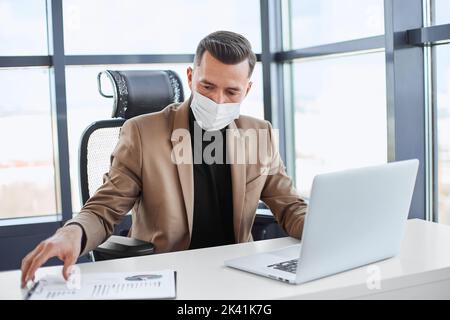 Geschäftsmann, der mit Finanzdokumenten an einem Laptop arbeitet. Stockfoto